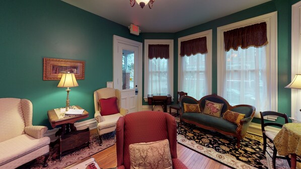 A room with teal walls, a red armchair, a green sofa, and a patterned rug.