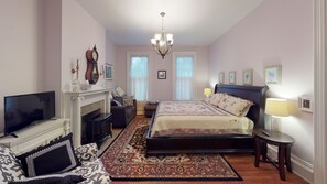Un dormitorio con cama, televisión, chimenea, candelabro y cuadros en la pared.