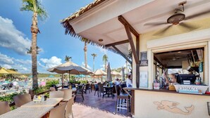 An outdoor dining area with tables and chairs, umbrellas, and a bar counter with a 'Welcome' sign. - Beach Getaway in Oceanside Resort (Fort Pierce)