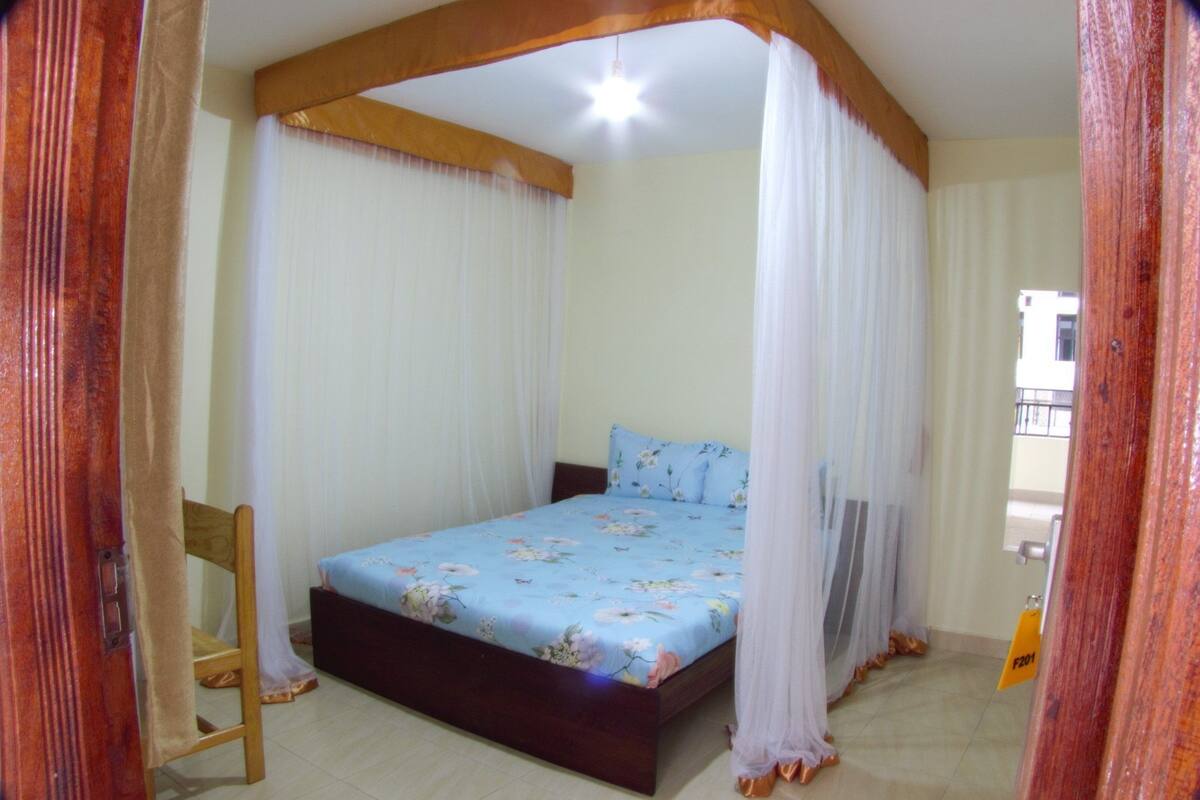 A bedroom with a bed, a wooden chair, and a canopy bed with sheer curtains.