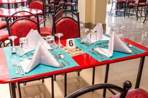 A dining table set with numbered place settings, red chairs, and a tiled floor. - The Fontage Hotel (Mlolongo)