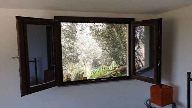 A room with a large window offering a view of a forested area. - Alicudi Apartment - 2 places (Reitano, MESSINA)