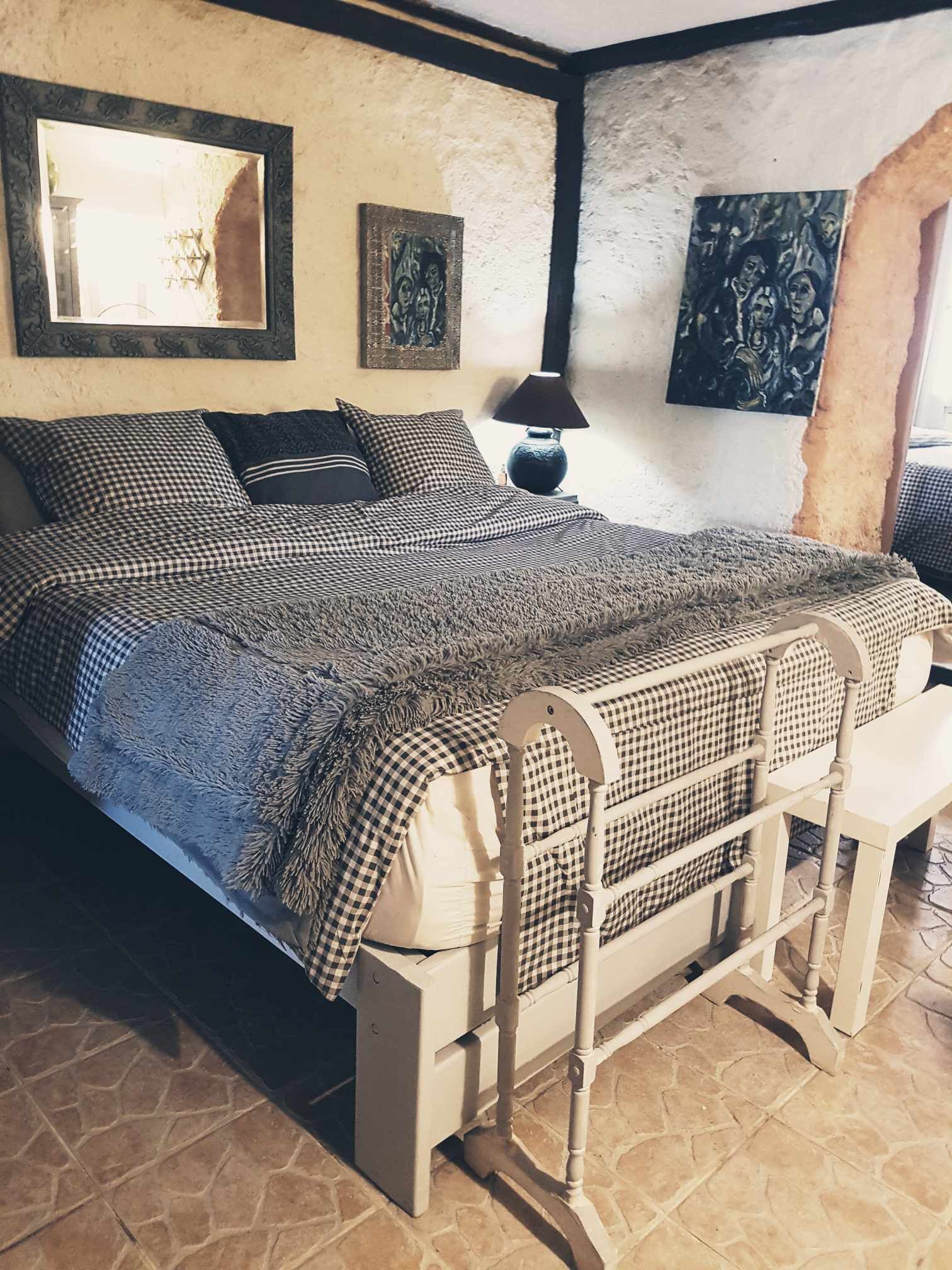 A bed with a checkered bedspread, a bedside table with a lamp, and artwork on the walls.