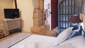 Una habitació amb un llit, una televisió sobre una petita taula, una làmpada i una finestra amb reixa metàl·lica.