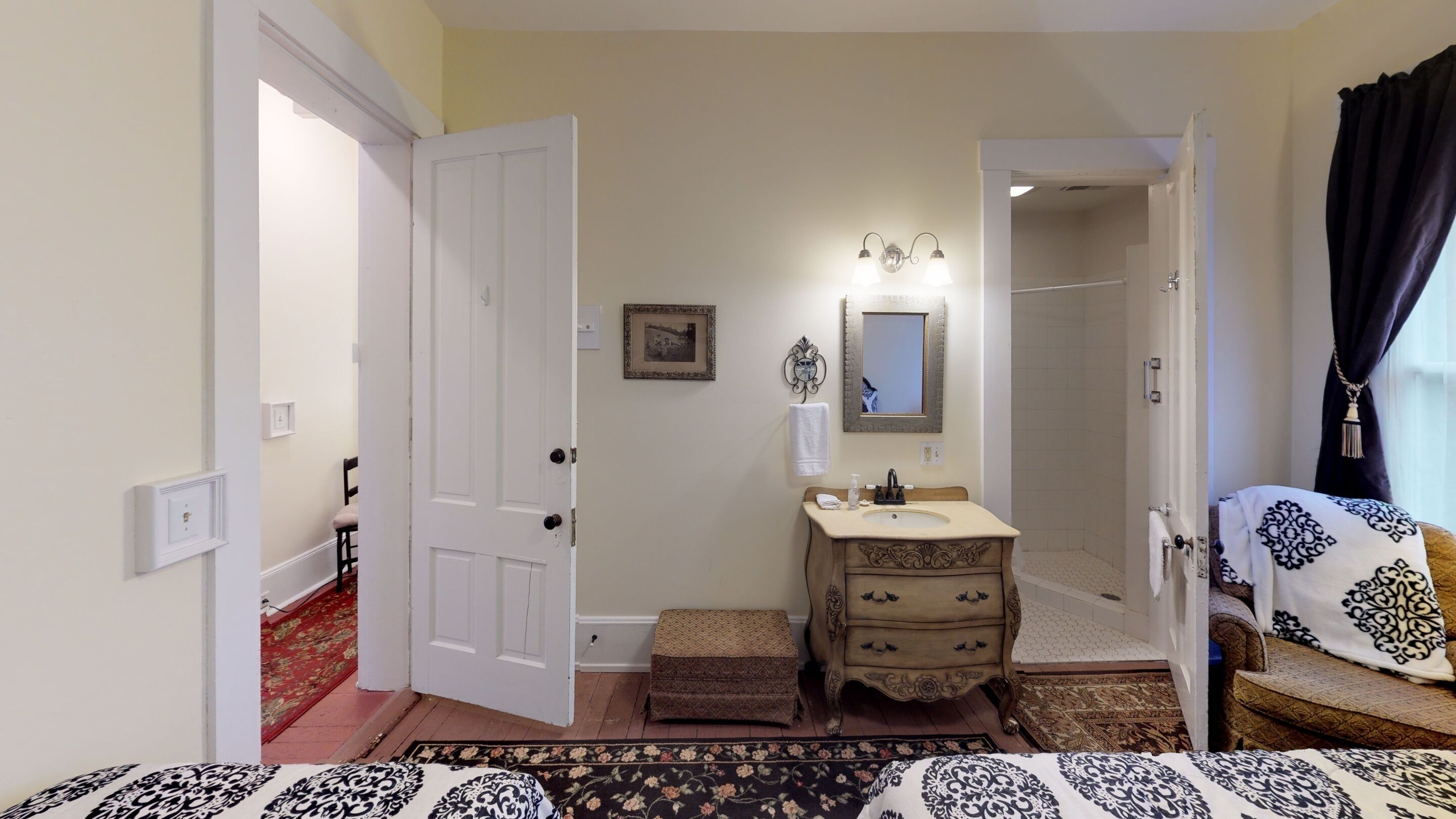 A bedroom with a bed, a bedside table, a dresser, a mirror, and a door leading to a bathroom.