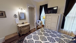 A hotel room with a bed, a dresser, a television, a bathroom with a shower, and a window with curtains.