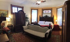 A room with a bed, a sofa, a wooden cabinet, a lamp, and a window with curtains.