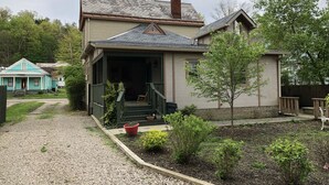 A two-story house with a front porch, a chimney, and a small garden with various plants.