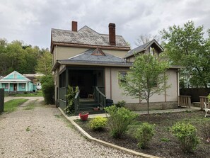 Una casa de un piso con porche, chimenea y un pequeño jardín con plantas en macetas.