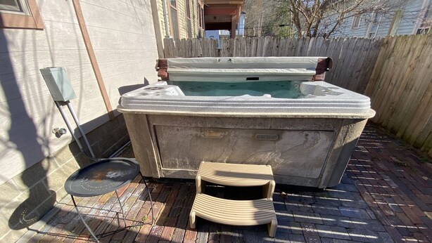 A hot tub in a backyard with a wooden deck, a small table, and a chair.