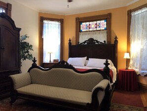 Una camera da letto con un letto grande, un'armadiatura in legno, un divano e una finestra con vetri colorati.