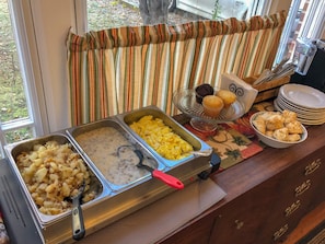 A buffet setup with various food items including potatoes, scrambled eggs, and muffins.