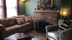 Una sala de estar acogedora con chimenea de ladrillo, sofá estampado con motivos florales y un sillón gris.