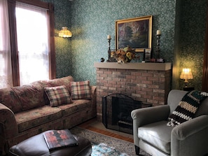 A cozy living room with a brick fireplace, floral-patterned sofa, and a grey armchair.