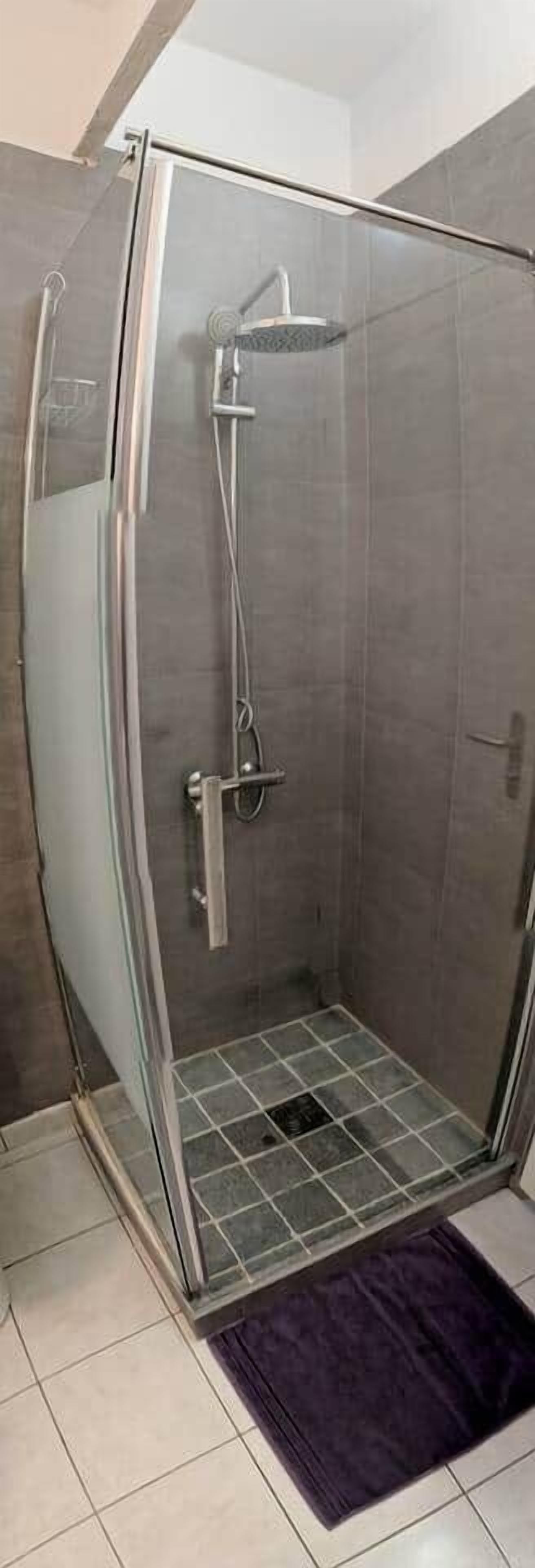 A glass-enclosed shower stall with a tiled floor and a purple rug.