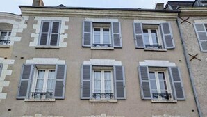 Un edificio de varios pisos con seis ventanas, cada una con contraventanas, y una puerta central.