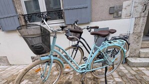 Una bicicleta azul claro con canasta y asiento marrón estacionada en una calle adoquinada.