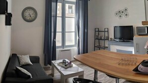 Una sala de estar moderna con sofá, mesa de centro, mesa de comedor de madera, televisión y zona de cocina.