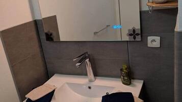 Un bagno moderno con lavandino bianco, specchio e porta asciugamani.
