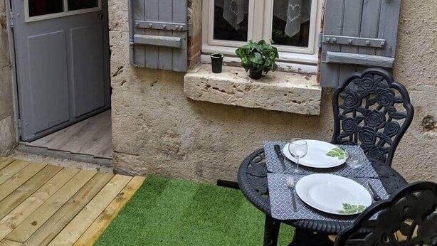 Un edificio de piedra con ventana, contraventanas, una puerta y una pequeña mesa con sillas.