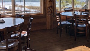 A wooden interior with large windows overlooking a body of water, featuring multiple dining tables and chairs. - Lake Texoma! Beautiful Cabin with Relaxing atmosphere!sleeps 5 (Gordonville)