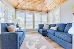 A room with a wooden ceiling, two blue sofas, a white rug with an anchor design, and a lamp on a side table. - Amazing Water Views, Short Walk to Duck and Beach! (Duck)