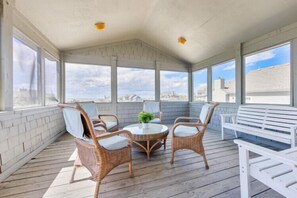 A covered outdoor seating area with wicker chairs, a white bench, and a round table with a potted plant. - Amazing Water Views, Short Walk to Duck and Beach! (Duck)