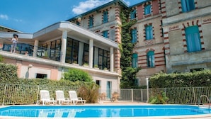 A hotel with a swimming pool, a covered balcony, and a historic building with striped walls and blue windows. - Charmant appartement entièrement équipé (ARCACHON)
