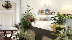 A reception area with a wooden reception desk, potted plants, a chandelier, and a wall-mounted shelf with various items. - Charmant appartement entièrement équipé (ARCACHON)