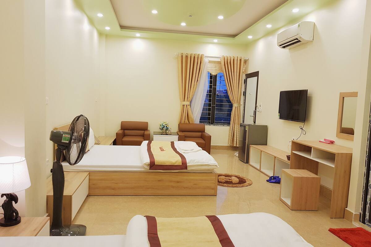 A hotel room with two beds, a desk, a chair, a TV, and an air conditioning unit.