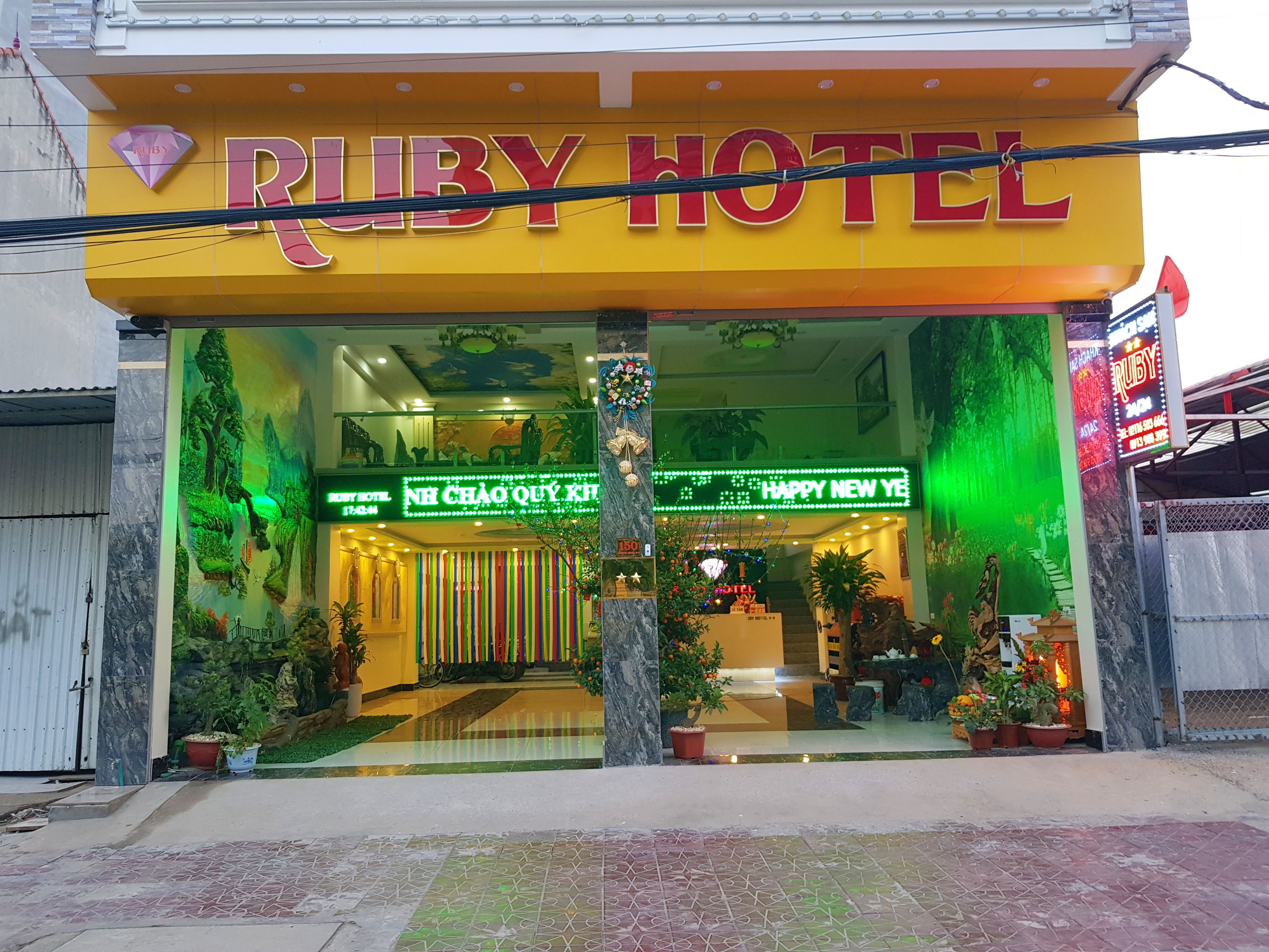 El Hotel Ruby con un cartel llamativo, una entrada iluminada en verde y un letrero festivo que dice 'Feliz Año Nuevo'.