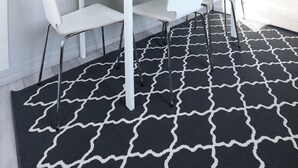 A modern room with a white table and chairs, a black and white patterned rug, and a blue floral painting on the wall. - Apartment Lali - Apartment with Balcony (Zadar)