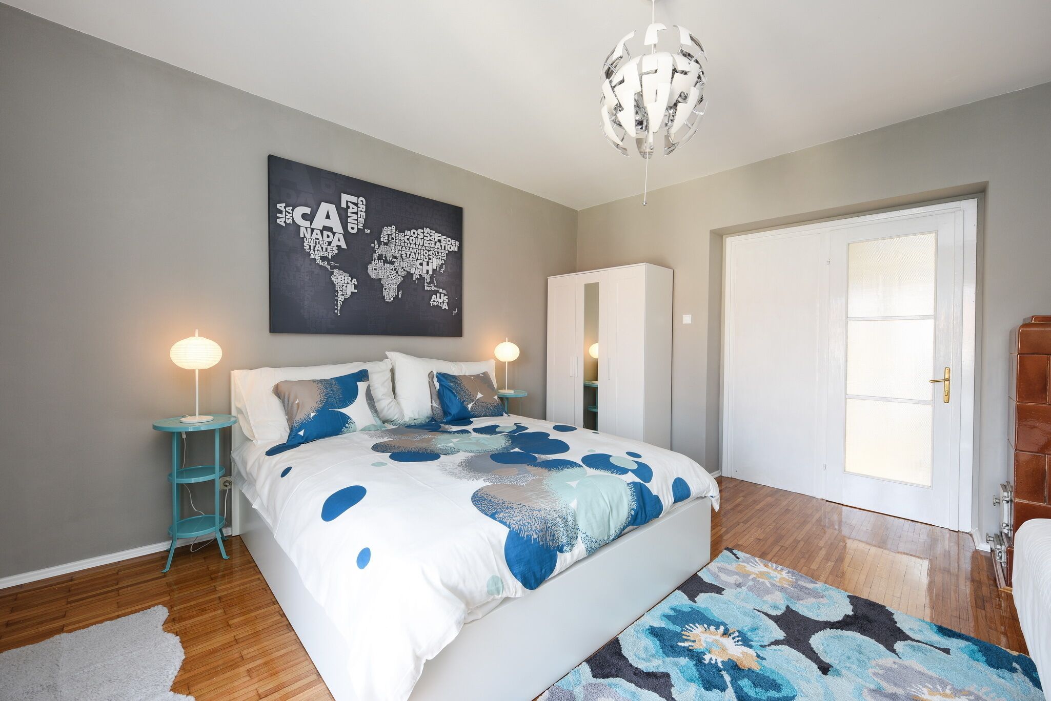 A bedroom with a bed, a map artwork, a wardrobe, a door, and a chandelier.