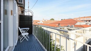 A balcony with a white chair, a metal railing, and a view of red-roofed buildings in the background. - Apartment Lali - Apartment with Balcony (Zadar)