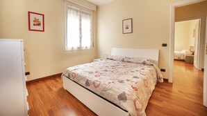 Ein Schlafzimmer mit Bett, einem Fenster mit Vorhängen, einer Tür zu einem anderen Raum und einer Wand-Klimaanlage.