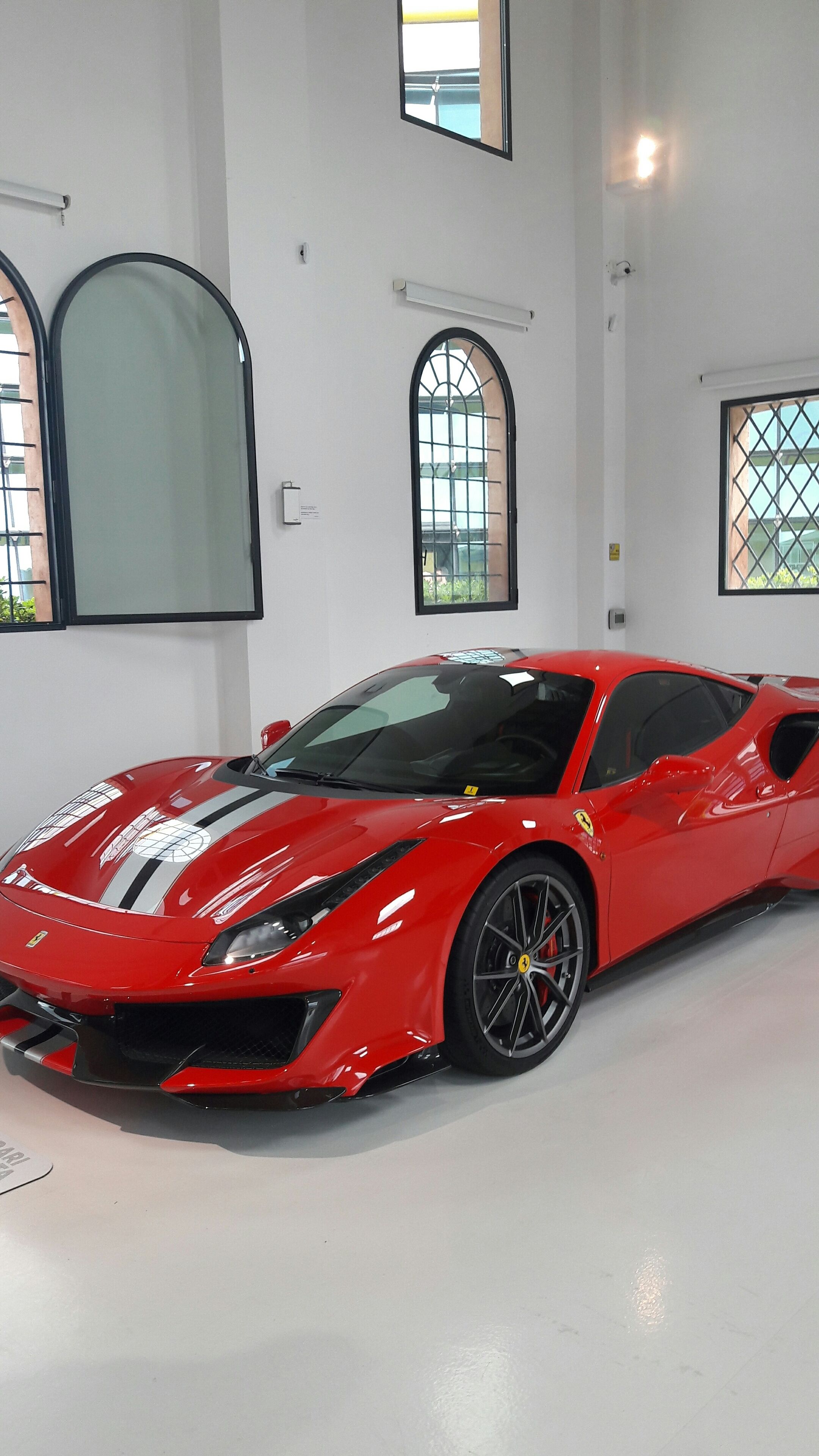Une voiture de sport rouge se trouve dans une pièce spacieuse et bien éclairée, dotée de grandes fenêtres et d’arcades.