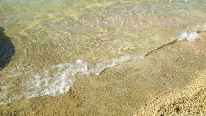 Una playa despejada con aguas poco profundas, un muelle y colinas al fondo.