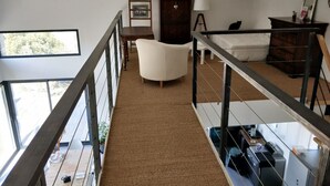 Amplia habitación con techo alto, un sofá blanco, un armario de madera y un escritorio con una impresora.