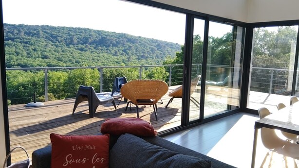 Habitación moderna con un ventanal grande, una terraza de madera y mobiliario exterior.
