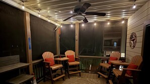 Een overdekt terras buiten met houten meubels, een plafondventilator en lichtslingers.