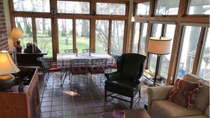 A cozy living room with a fireplace, a dining area with a table and chairs, and large windows offering a view of the outdoors. - Nancy’s Touch, A Waterfront Paradise! (North East)