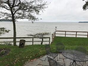 Une terrasse au bord du lac, avec une table et des chaises en métal, une clôture en bois et un arbre.