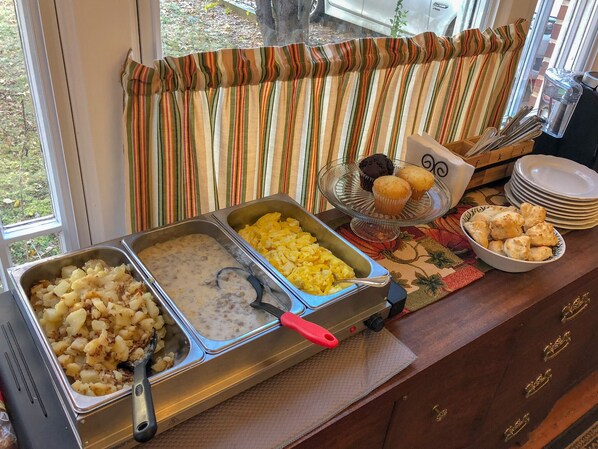 A buffet setup with various food items including potatoes, scrambled eggs, and muffins.