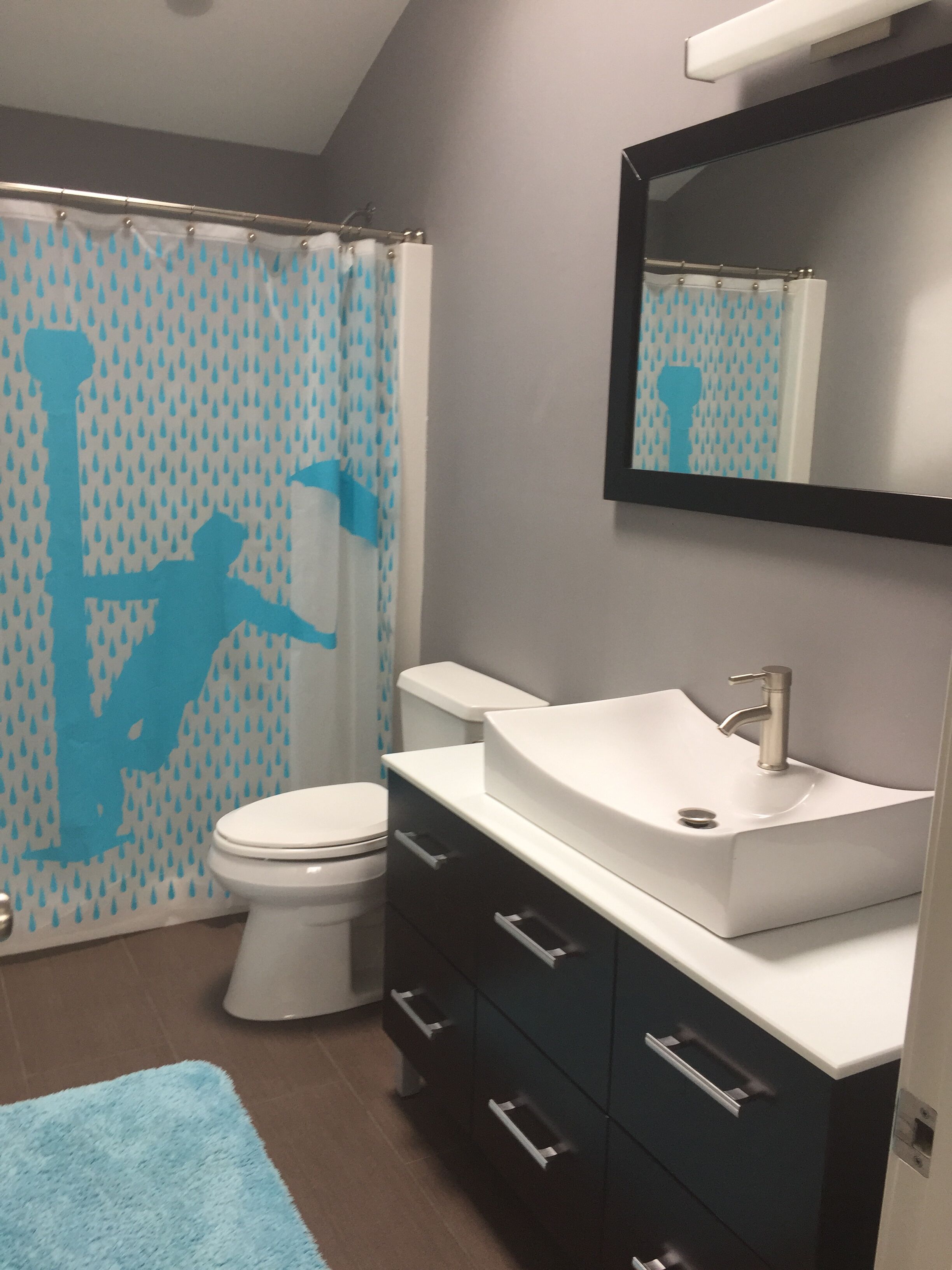 A bathroom with a shower curtain, toilet, sink, and cabinet.