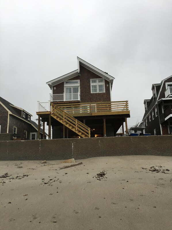 A two-story wooden house with a balcony and a wooden staircase leading to the upper floor. - Oceanfront/ Beachfront Home on Sand Hills Scituate (Scituate)