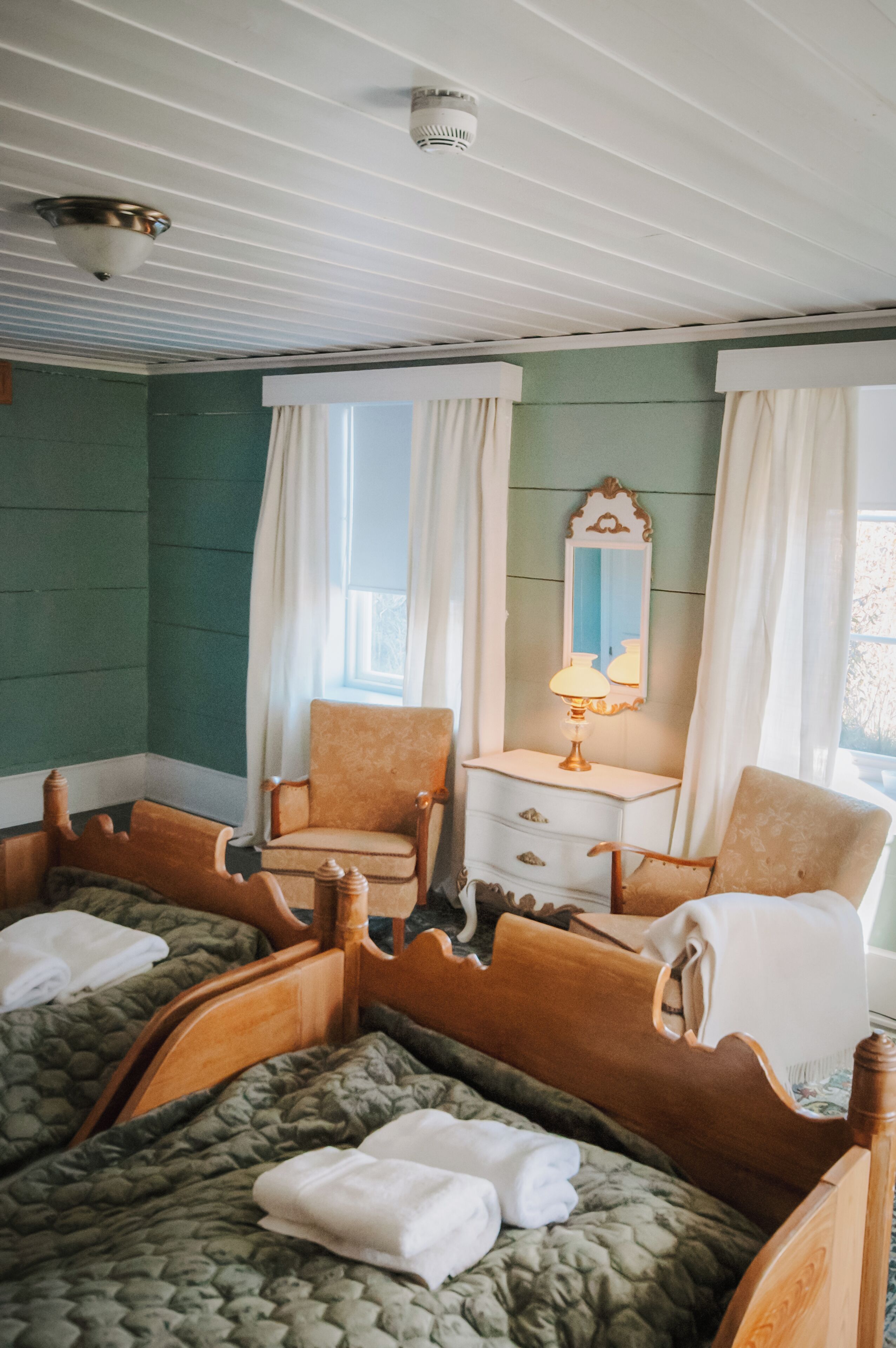 A room with two wooden beds, a chair, a dresser, and a mirror.