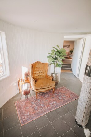 A corner room with a large, plush armchair, a potted plant, a small side table with a lamp, and a patterned rug.