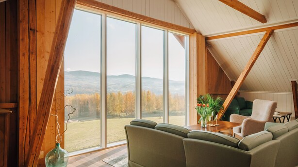 Una habitación acogedora con un ventanal grande, un sofá verde y un techo de madera.