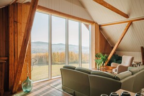 A cozy room with a large window, a green sofa, and a wooden ceiling. - Helgaker Gård (Gran)