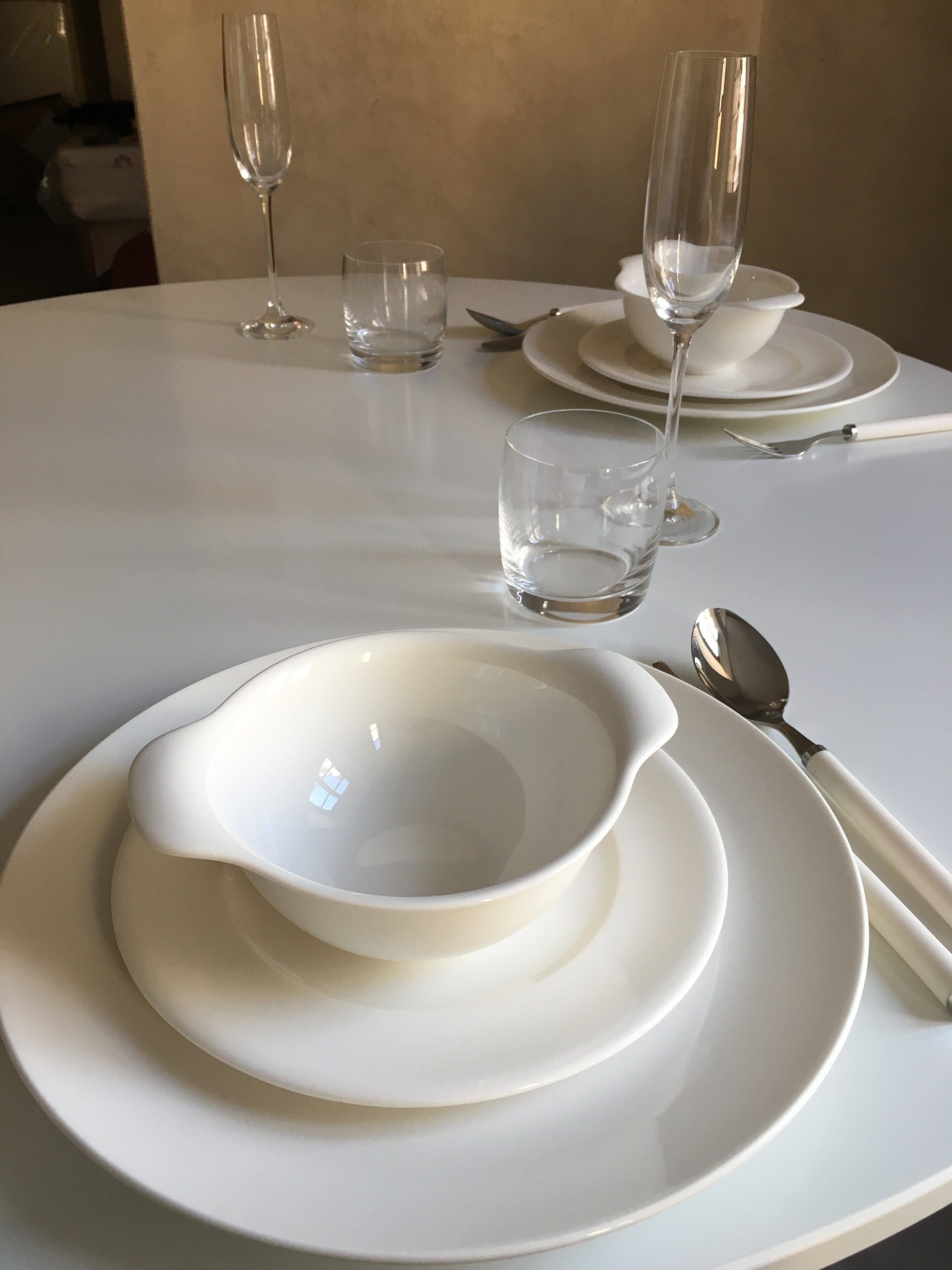 A table set with white plates, bowls, and cutlery, including a spoon and a glass.
